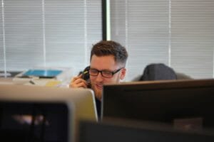 A man making a call on a cell phone behind his desk