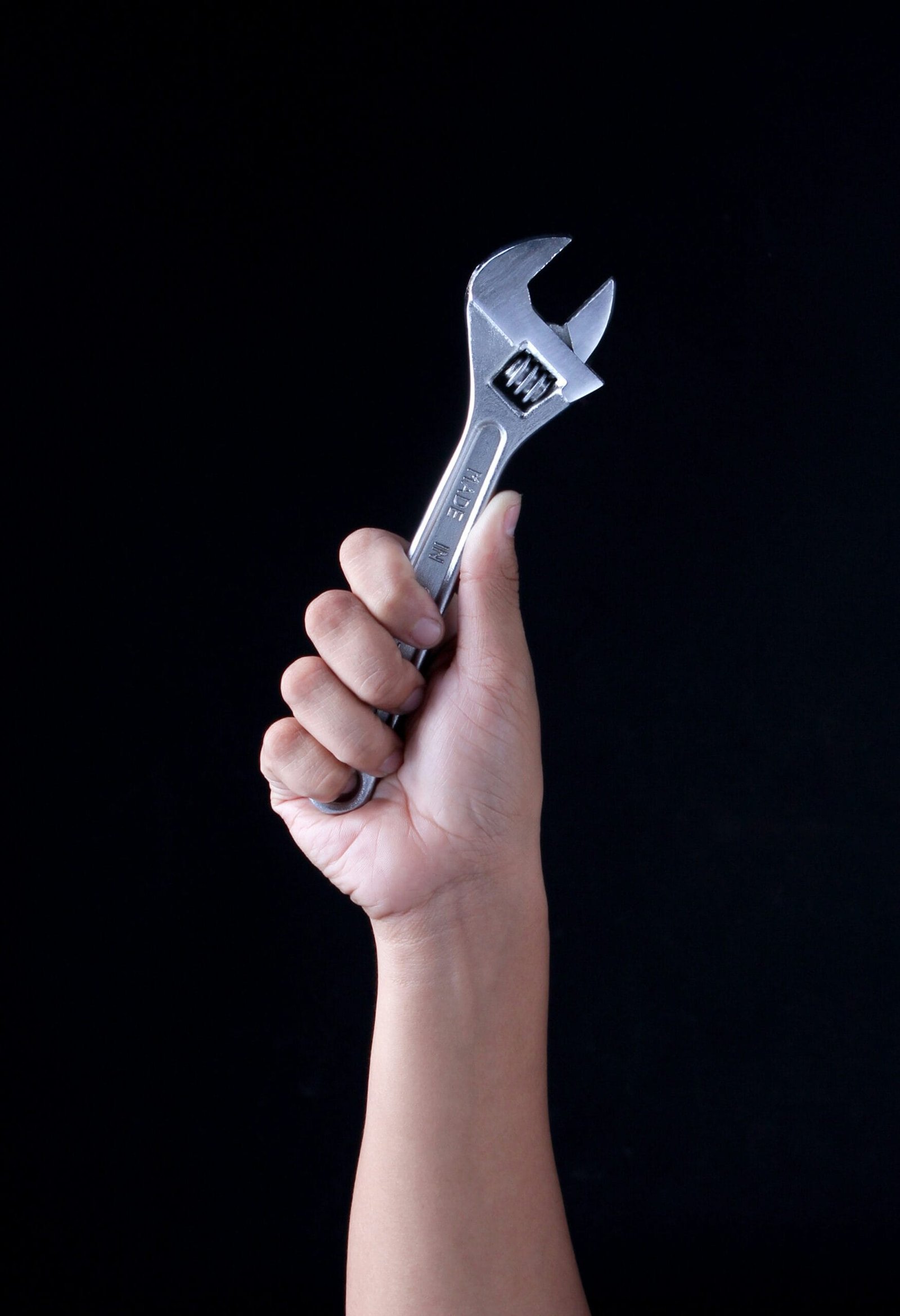 A hand holding a wrench triumphantly on a black background. Photo by Recha Oktaviani on Unsplash