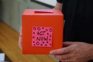 A person holds a red box with a sticker that says "ACT NOW". Photo by Jo Szczepanska on Unsplash