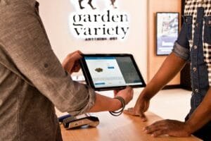 A budtender and customer discuss the merits of various cultivars in a dispensary. Between them is a lit tablet. Photo by Cova Software on Unsplash