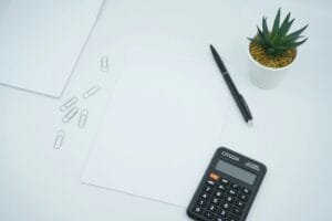 A financial and money themed photo featuring a blank paper on a desk next to a pen and calculator. Photo by Mediamodifier on Unsplash