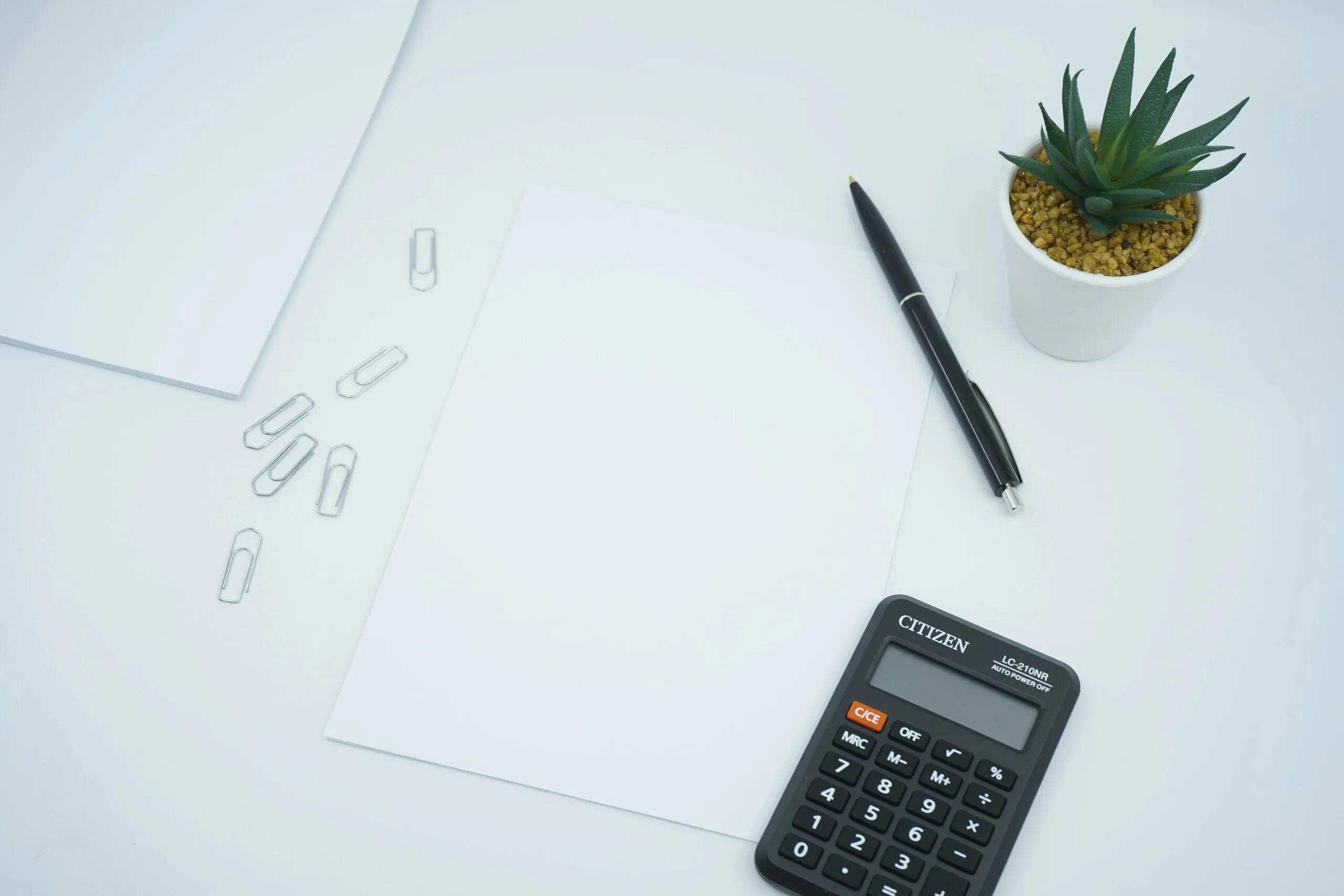 A financial and money themed photo featuring a blank paper on a desk next to a pen and calculator. Photo by Mediamodifier on Unsplash