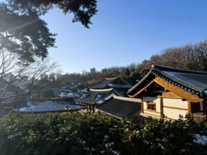 A view of a Korean Buddhist temple through snowy bushes in winter, and a blue sky above