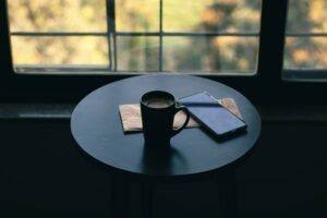 A cup of coffee and a cell phone on a desk in front of windows. Photo by VD Photography on Unsplash