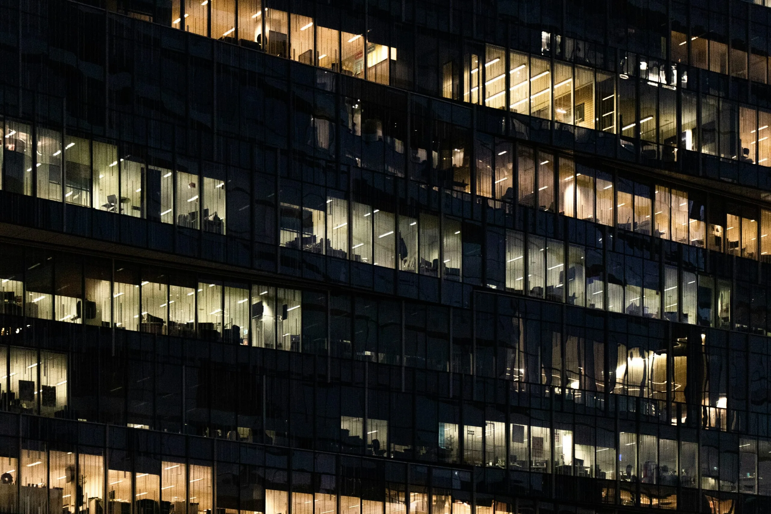 View from the street of curtain glass windows of an office building still busy at night. Photo by Mitchell Luo on Unsplash
