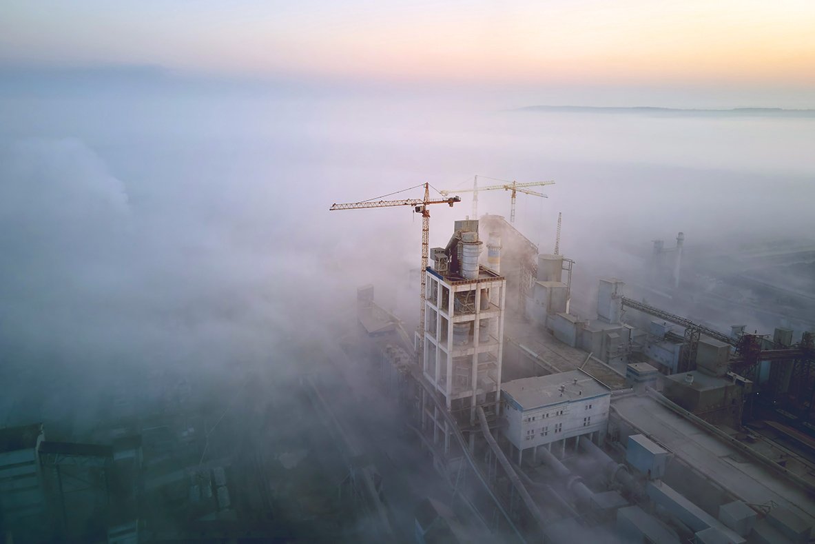 A construction crane rises above fog at an industrial site at dawn