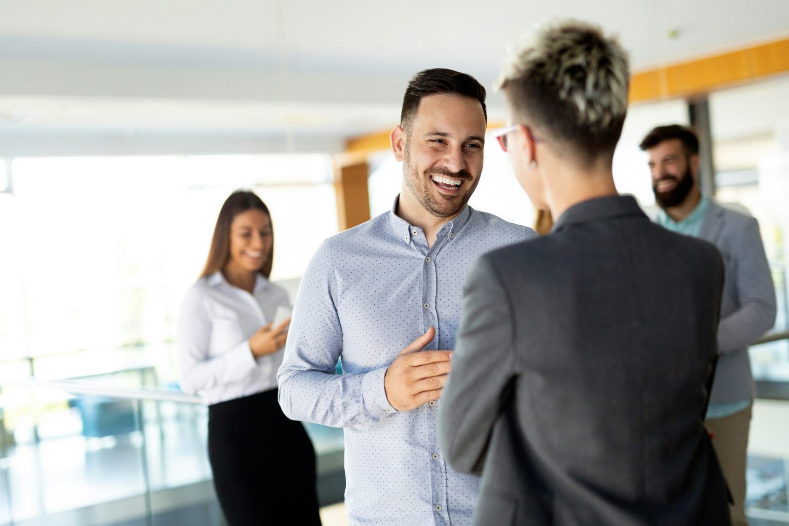 A sales guy with a skim beard closing a deal at a workplace with employees in the background. Photo credit Getty Images on Unsplash.